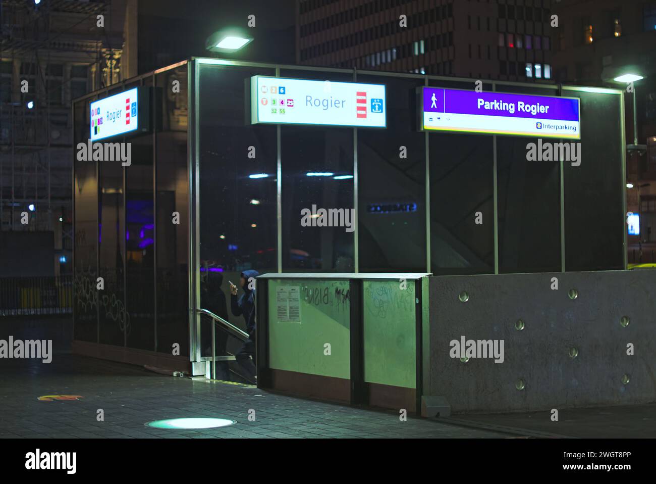 Bruxelles, Belgio. 5 febbraio 2024. Ingresso alla metropolitana. Passeggero al telefono in metropolitana di notte. Stazione Roger. Grattacielo sullo sfondo Foto Stock