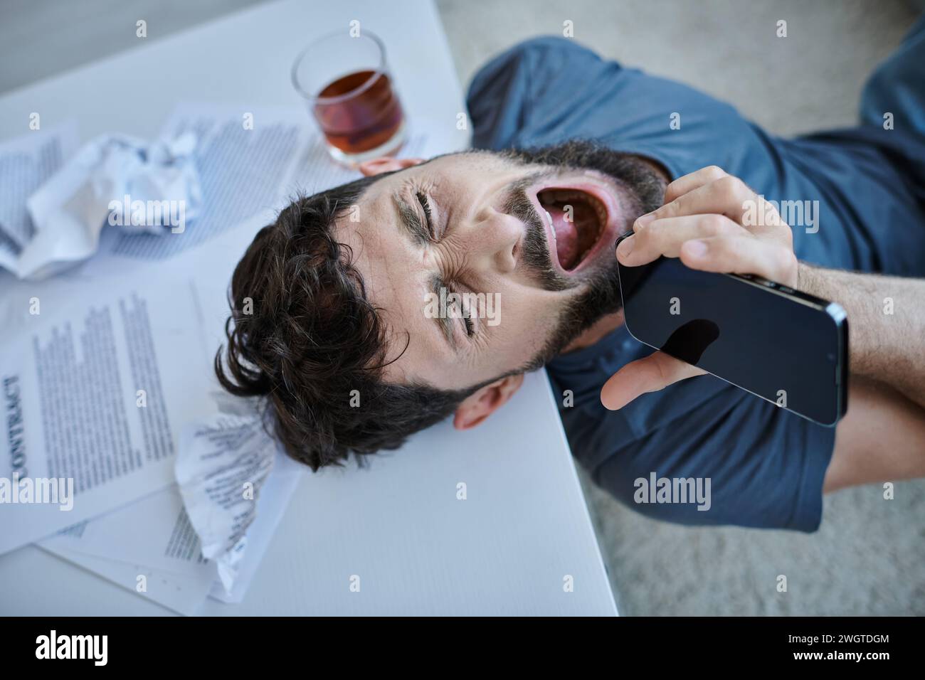 uomo frustrato urlando allo smartphone con un bicchiere di alcol accanto a lui durante un crollo mentale Foto Stock
