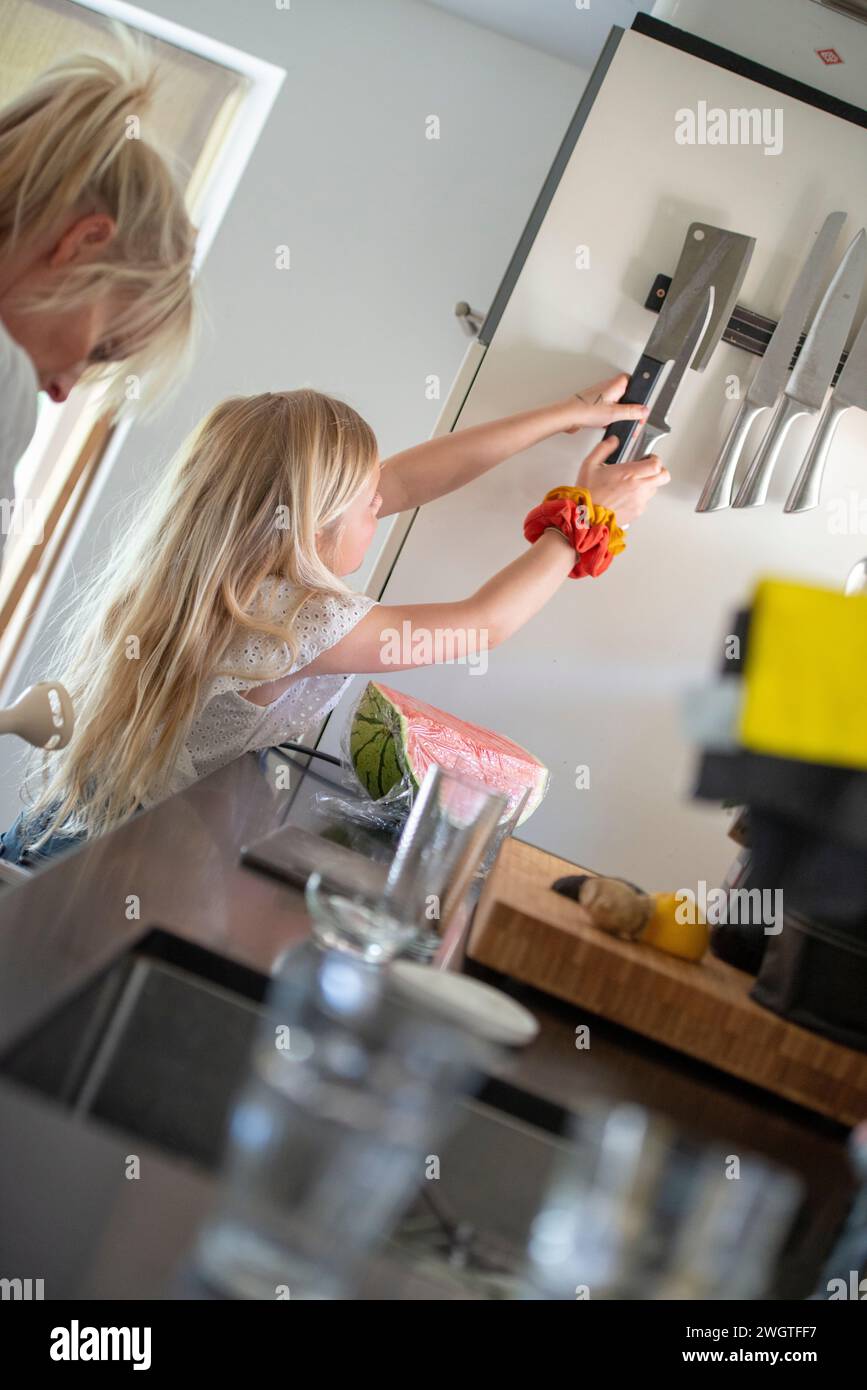 Giovane ragazza in cerca di un coltello affilato, aiutata da sua madre ad essere pulita e sicura Foto Stock