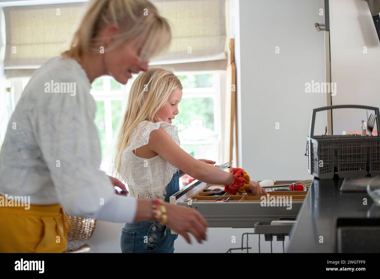 Giovane ragazza in cerca di un coltello affilato, aiutata da sua madre ad essere pulita e sicura Foto Stock