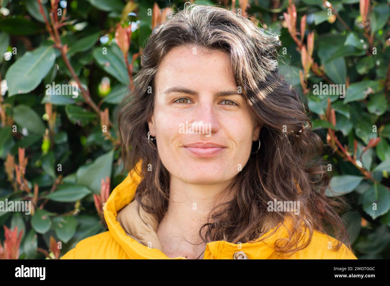 giovane donna in piedi fuori, sorridente davanti alle foglie Foto Stock