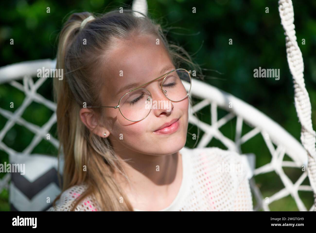 Giovane adolescente bionda seduto al sole, godendosi i raggi e rilassandosi. Immergiti nella pace e nella tranquillità Foto Stock