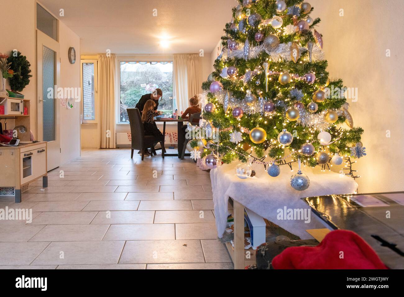 La famiglia sedeva al tavolo scrivendo auto con l'albero di Natale in primo piano. Luci e baule Foto Stock