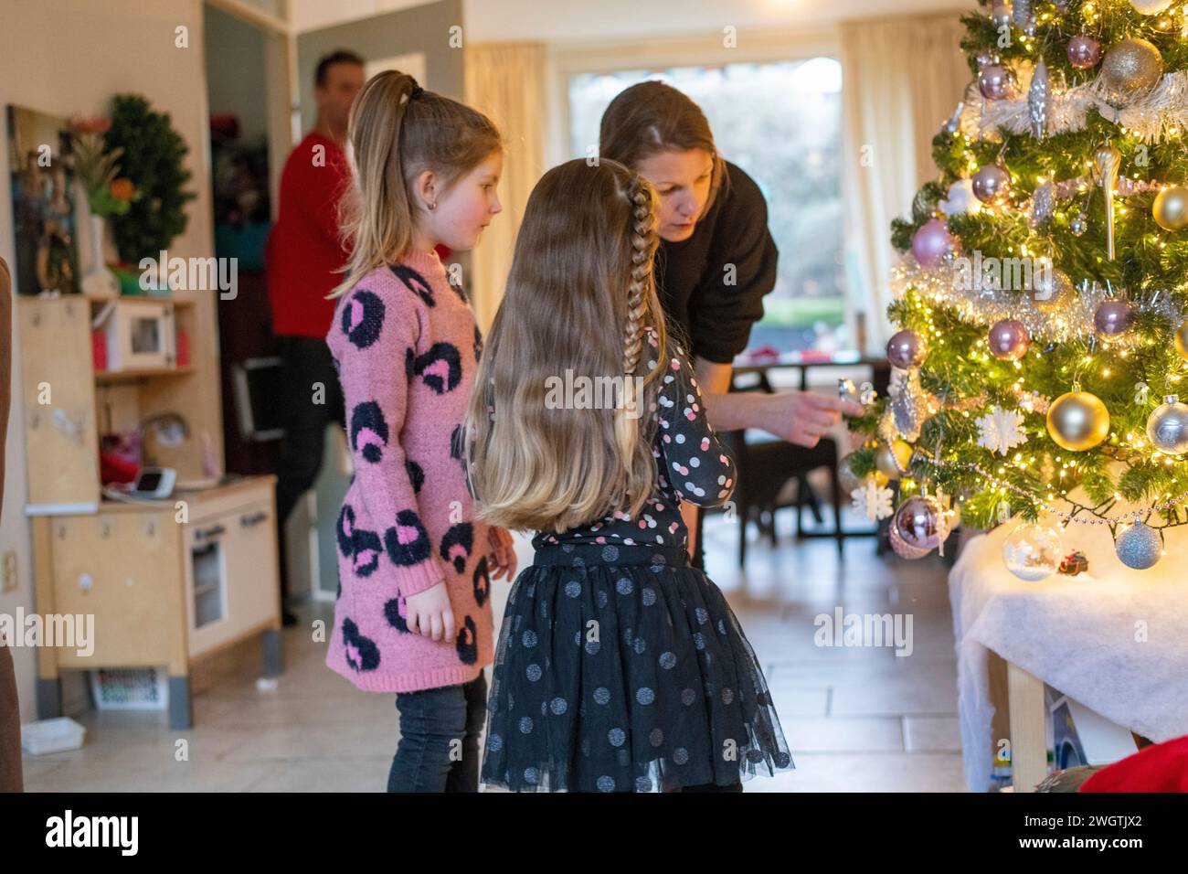 Mamma single che aiuta le sue figlie a mettere gli ornamenti sul loro albero. Un bellissimo momento di legame con luci scintillanti e baule. Foto Stock