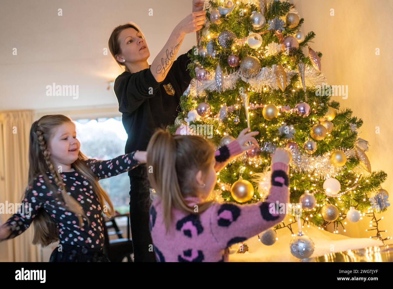 Mamma single che aiuta le sue figlie a mettere gli ornamenti sul loro albero. Un bellissimo momento di legame con luci scintillanti e baule. Foto Stock
