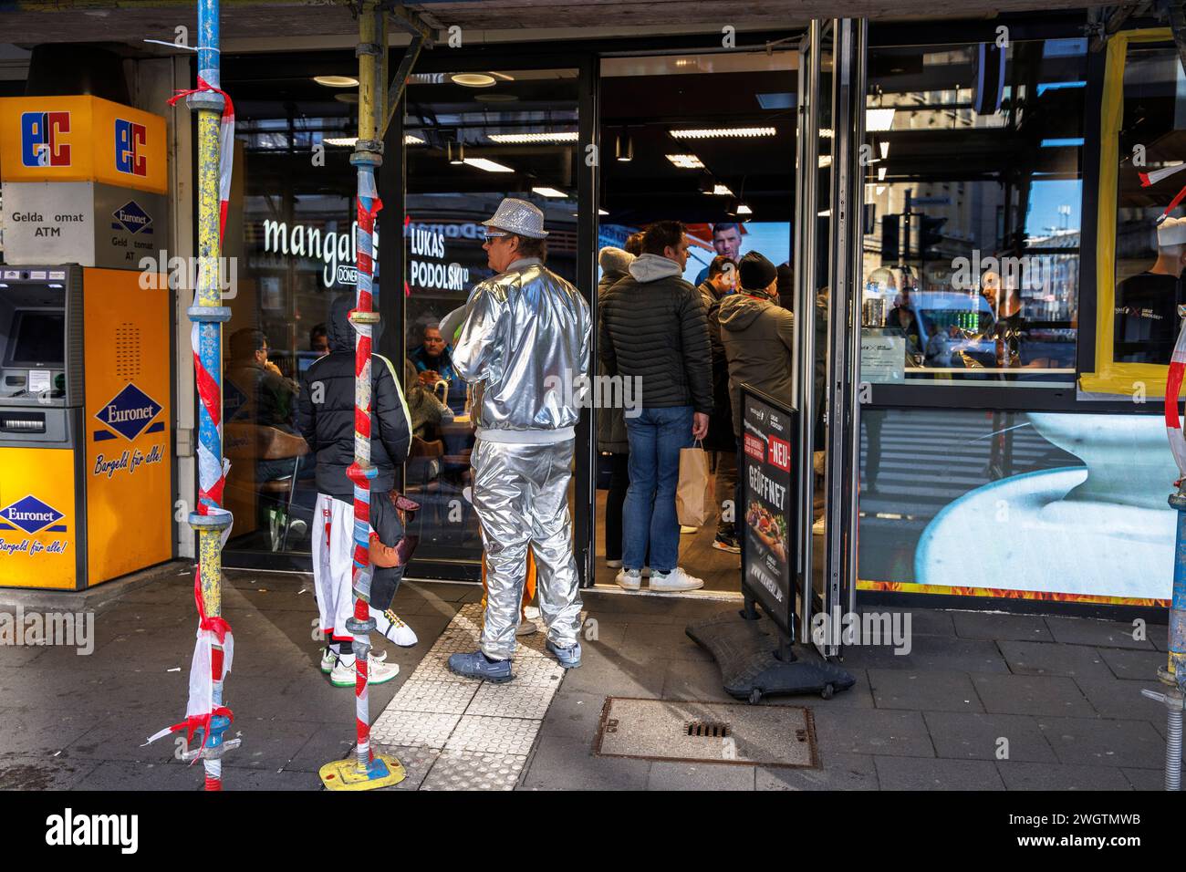 Man indossa un costume d'argento di fronte a un ristorante Mangal Doener in via Komoedien, vicino alla cattedrale di Colonia, Germania. Mann steht in einem si Foto Stock