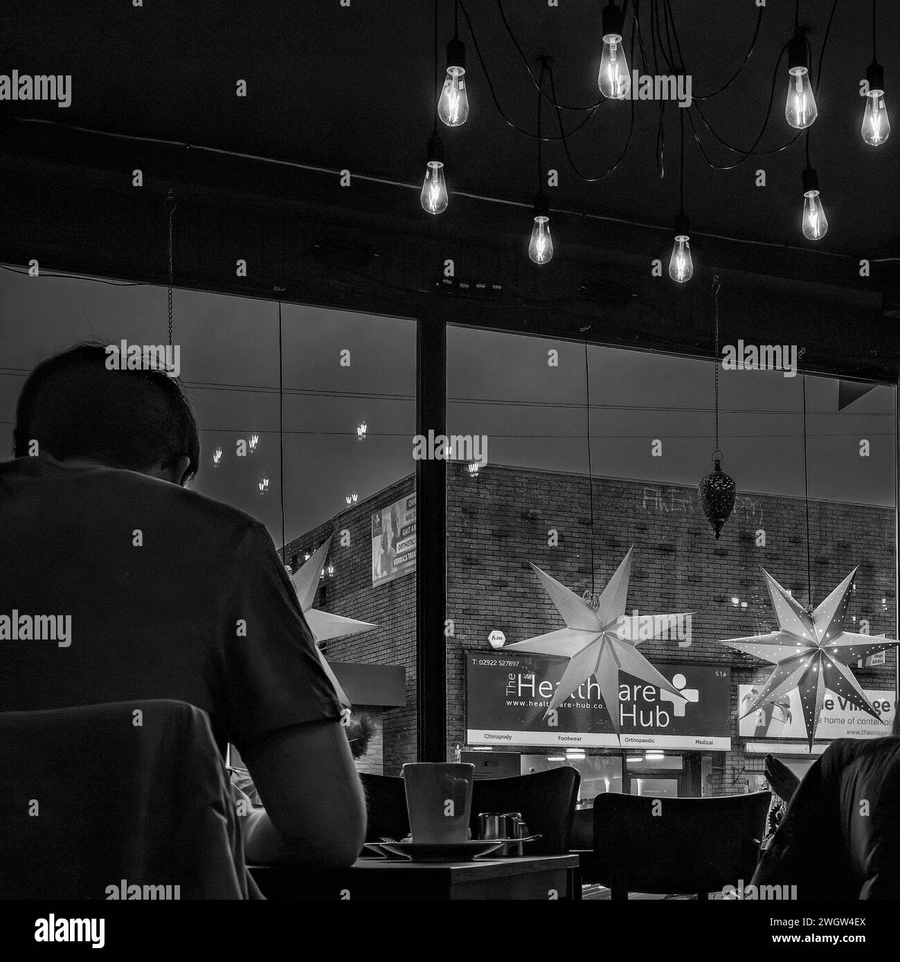 Uomo seduto in un bar colorato la sera, guardando il suo telefono, aspettando qualcuno. Immagine in bianco e nero a contrasto elevato. Foto Stock