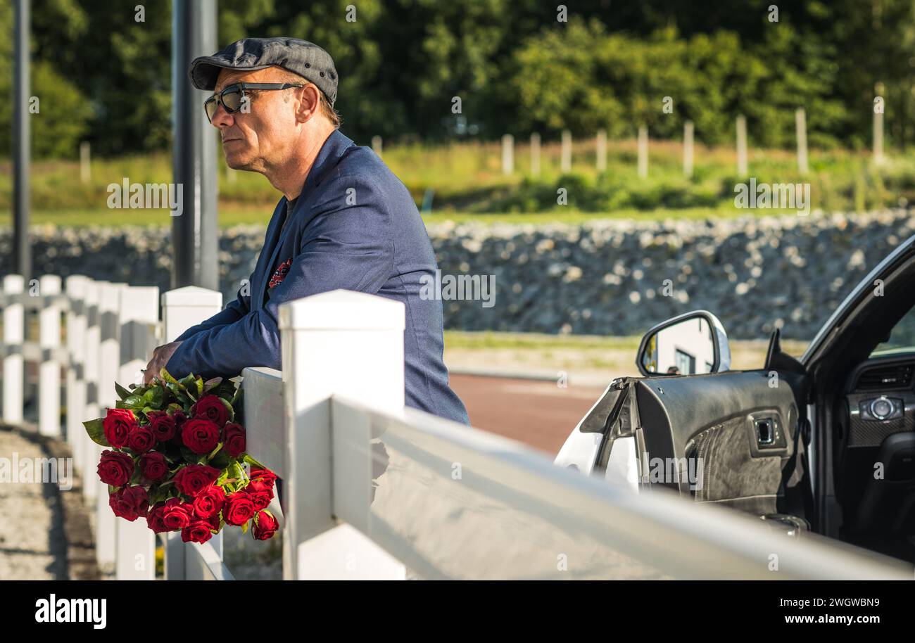 Romantico Caucasico Senior nei suoi 60 anni con le rose rosse in mano in attesa del suo appuntamento Foto Stock