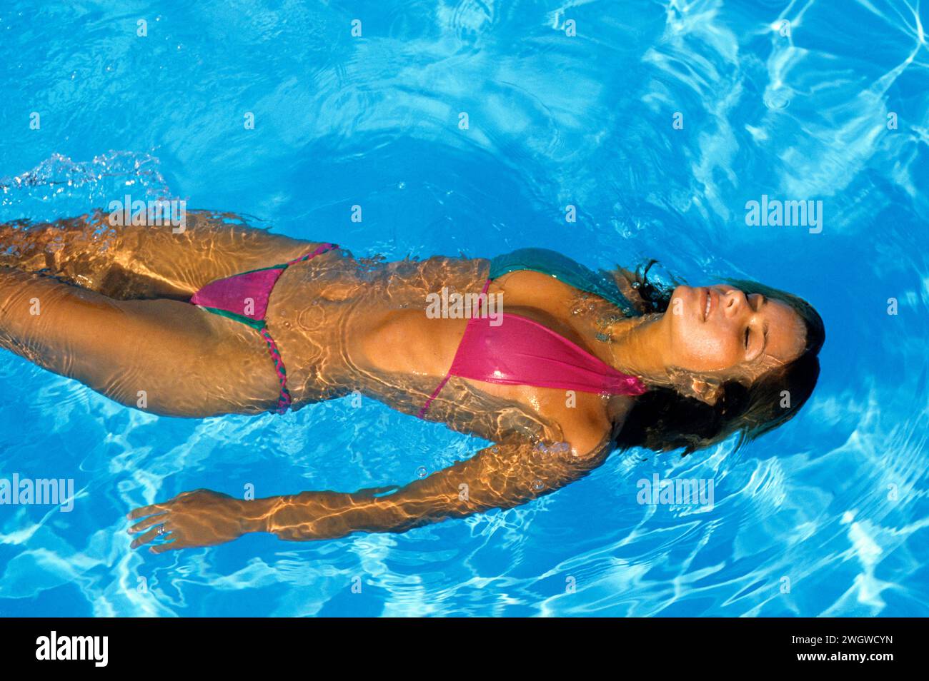 Giovane donna capelli scuri che nuota sulla fotocamera posteriore anteriore sullo sfondo della piscina Foto Stock