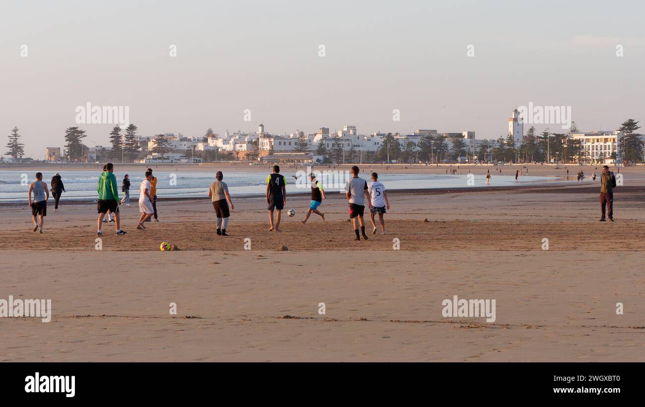 Una sera i giovani giocano a calcio su una spiaggia sabbiosa con la storica Medina alle spalle a Essaouira, Marocco, 6 febbraio 2024 Foto Stock