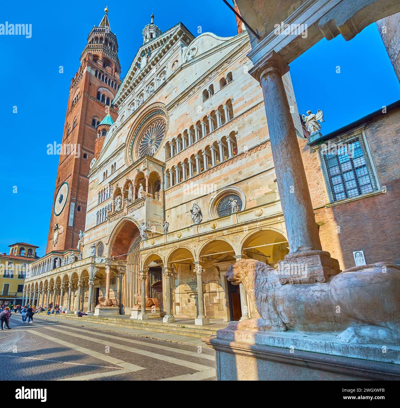 La facciata medievale e il campanile Torrazzo della Cattedrale di Cremona dietro il leone in pietra e il pilastro del portico del Battistero, Italia Foto Stock