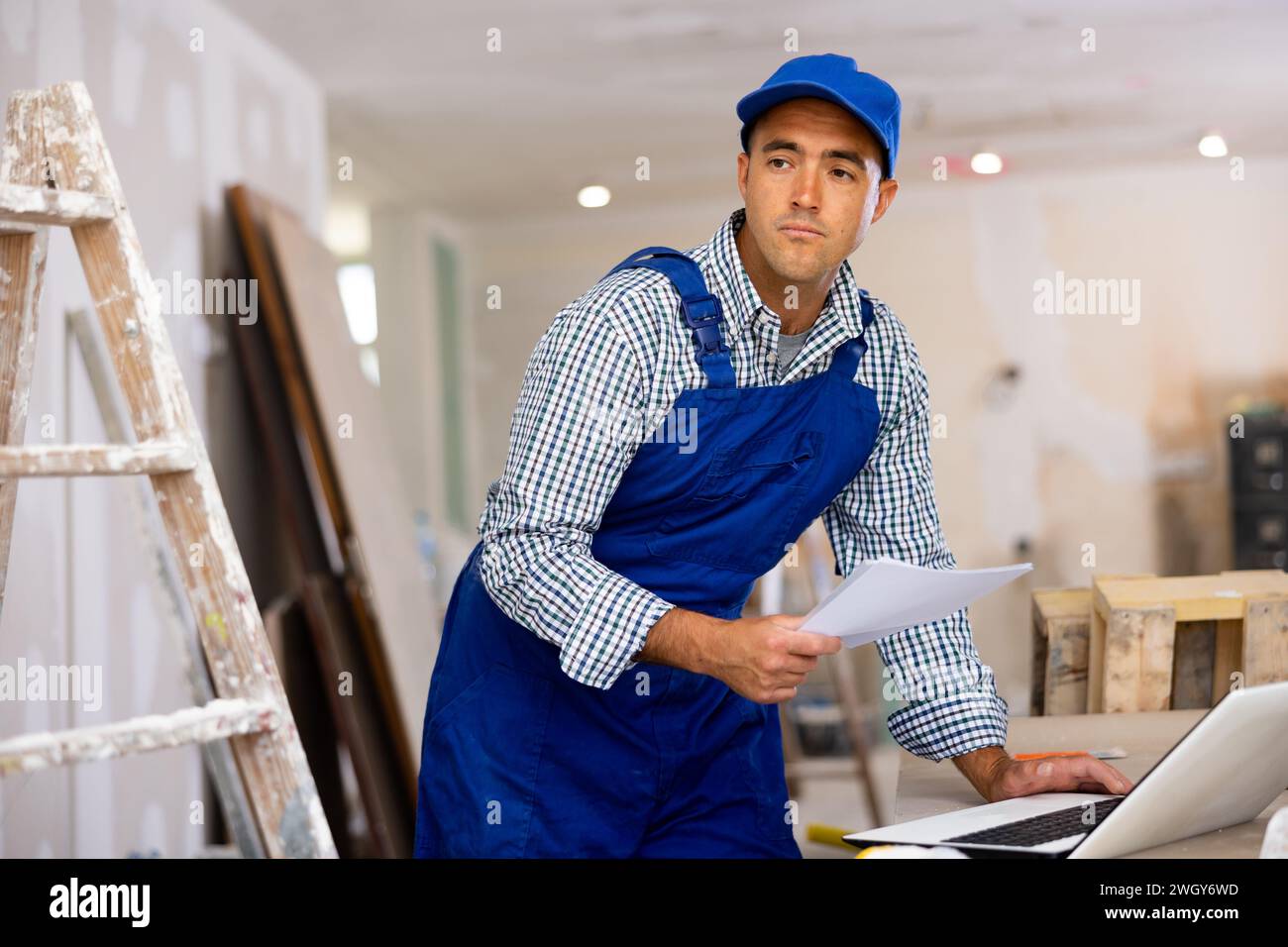 Man engineer che controlla i documenti e utilizza il computer portatile durante gli interventi di riparazione Foto Stock