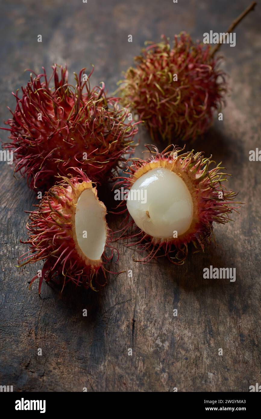 primo piano di rambutan maturo, sbucciato e frutta tropicale intera succosa originaria del sud-est asiatico, sparsi su un piano da tavolo in legno, messa a fuoco morbida con spazio copia Foto Stock