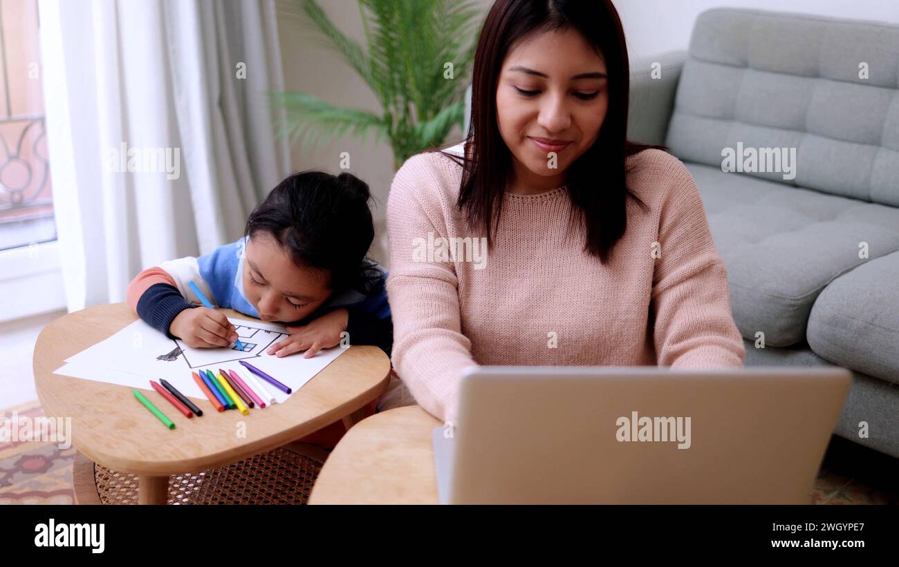 Madre asiatica che si prende cura del suo bambino dipingendo mentre usa il computer portatile a casa. Vita familiare tyle Foto Stock