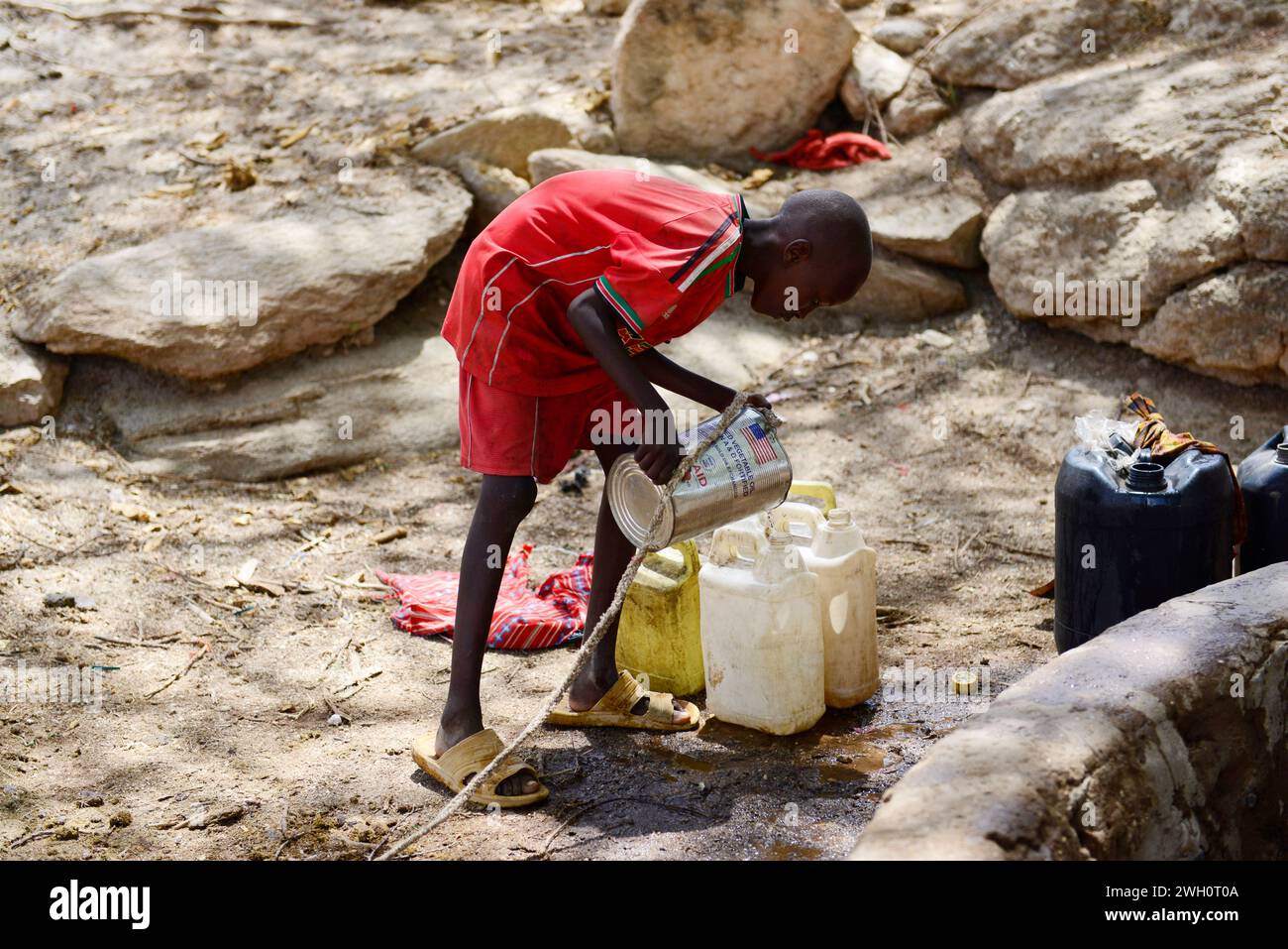 Un ragazzo che riempie le taniche d'acqua in un pozzo aperto a Ngurunit, in Kenya. Foto Stock