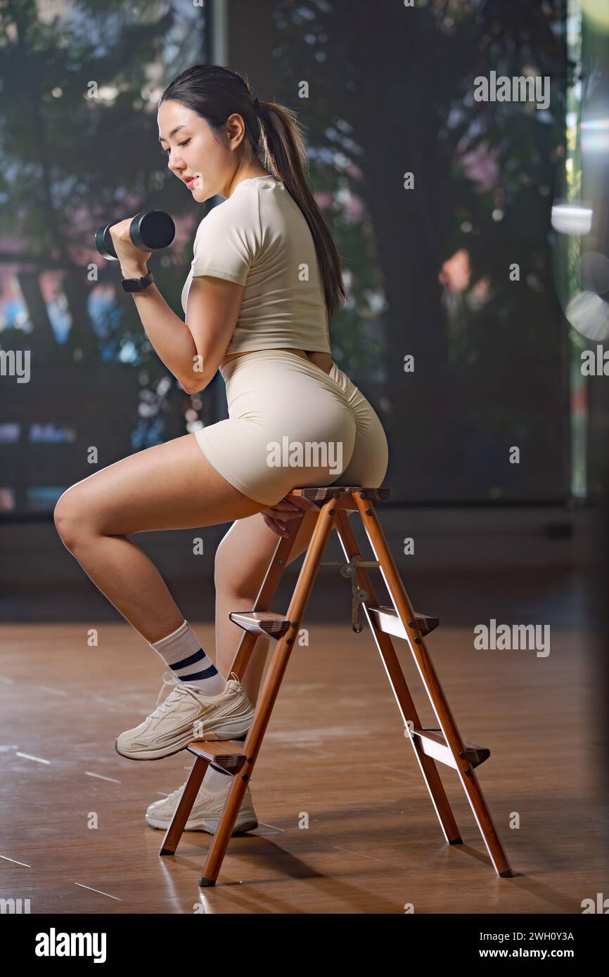 Fitness donna asiatica che fa esercizio fisico e solleva i pesi dei manubri nella palestra sportiva. Foto Stock