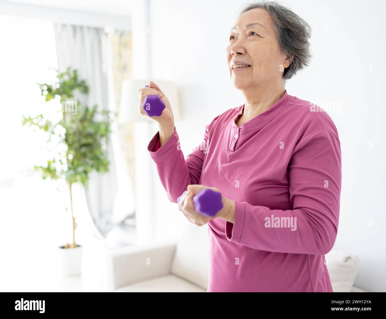 Donna asiatica anziana che fa esercizi con manubri al chiuso. Foto Stock