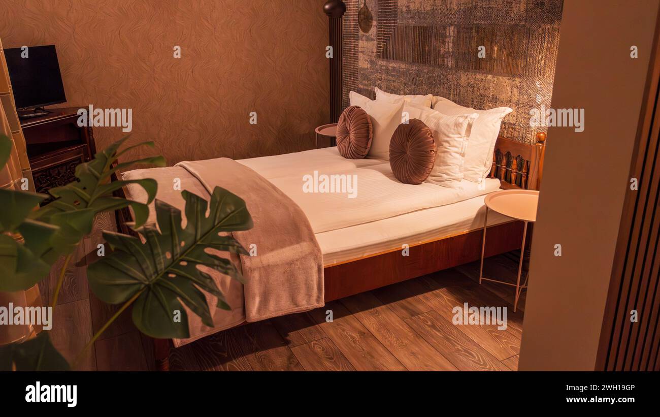Un grande letto con cuscini in una camera d'hotel con tv e piante Foto Stock