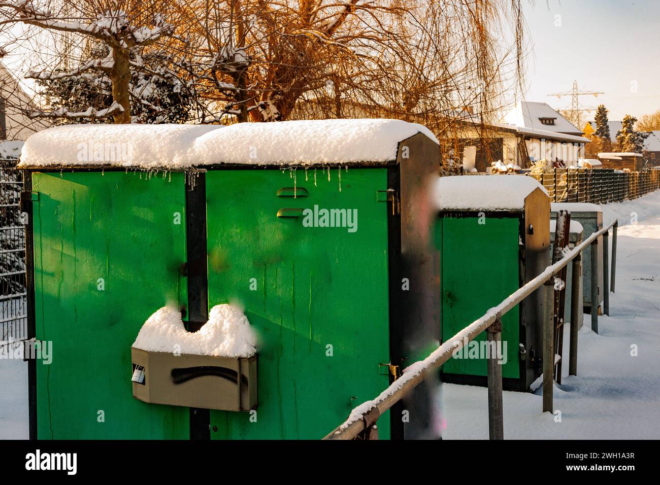Scatola di derivazione elettrica chiusa con accumulo di neve pesante sulla parte superiore accanto ai binari, metallo verde, alberi nudi ed edifici sullo sfondo, wi-fi soleggiato Foto Stock