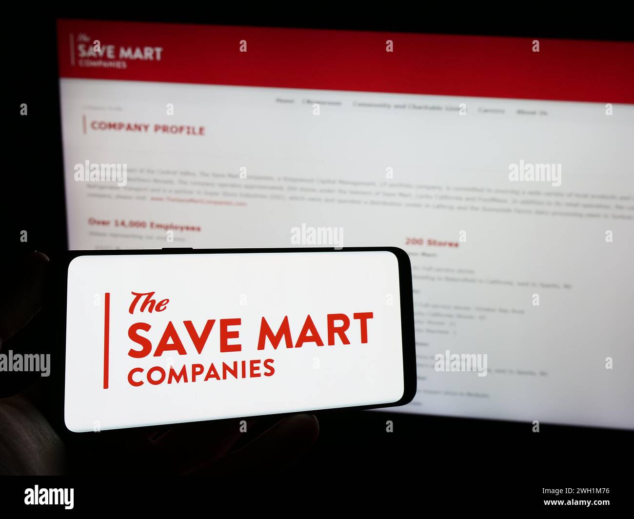 Persona che detiene un telefono cellulare con il logo della società americana di supermercati The Save Mart Companies davanti alla pagina web. Mettere a fuoco il display del telefono. Foto Stock