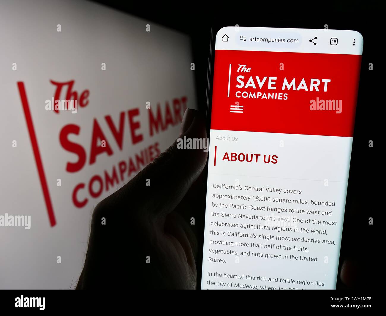 Persona che detiene un telefono cellulare con il sito web della società di supermercati statunitense The Save Mart Companies davanti al logo. Messa a fuoco al centro del display del telefono. Foto Stock