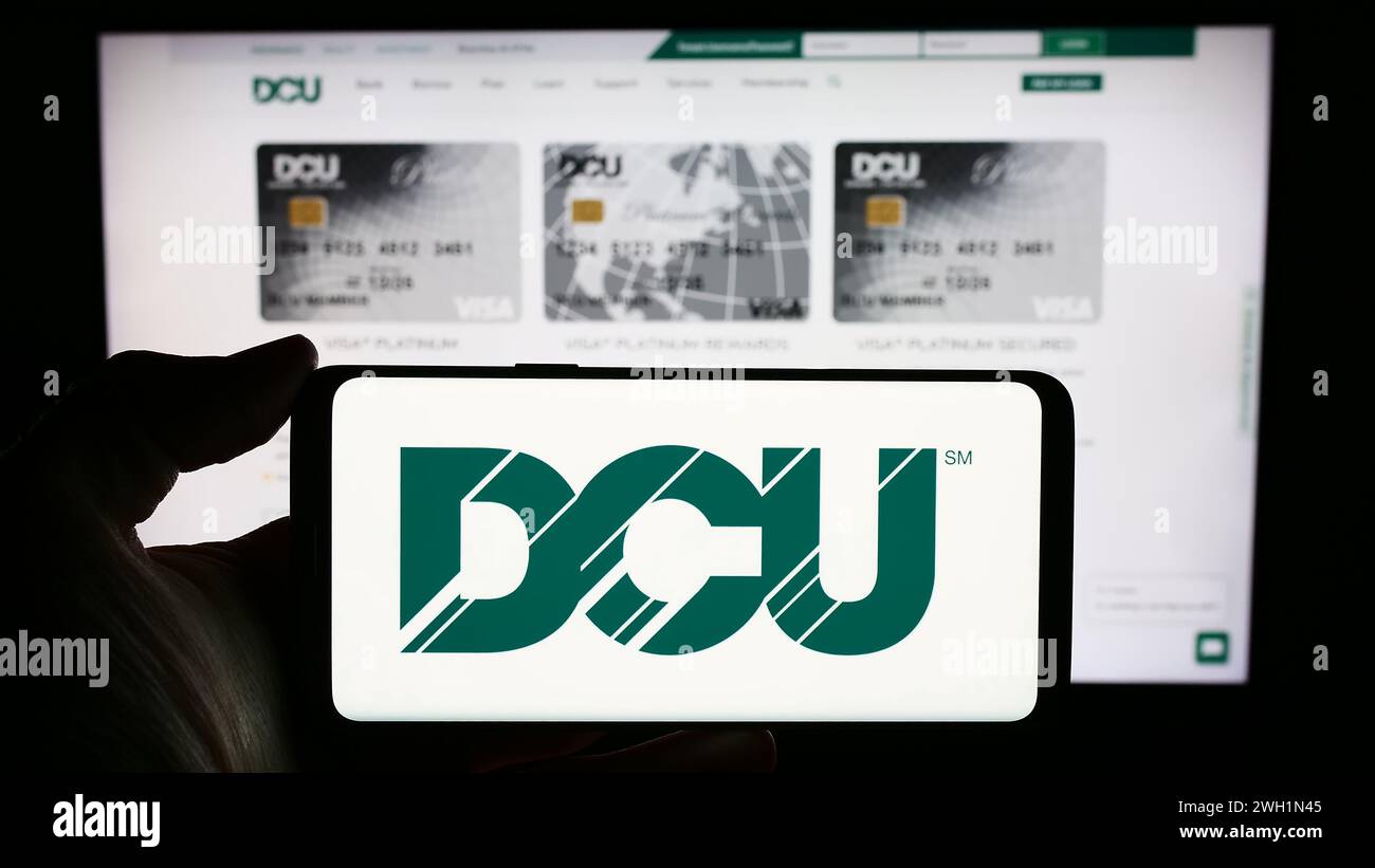 Persona che detiene un cellulare con il logo dell'istituto finanziario Digital Federal Credit Union (DCU) davanti alla pagina Web. Mettere a fuoco il display del telefono. Foto Stock