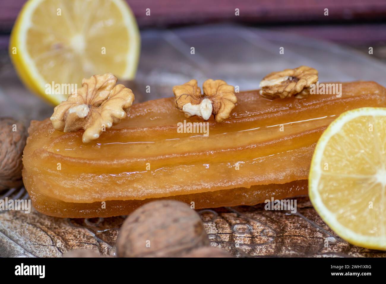 Torta dolce turca chiamata tulumba, servita al piatto con fette di limone e noci intorno, su un enorme tavolo di legno Foto Stock