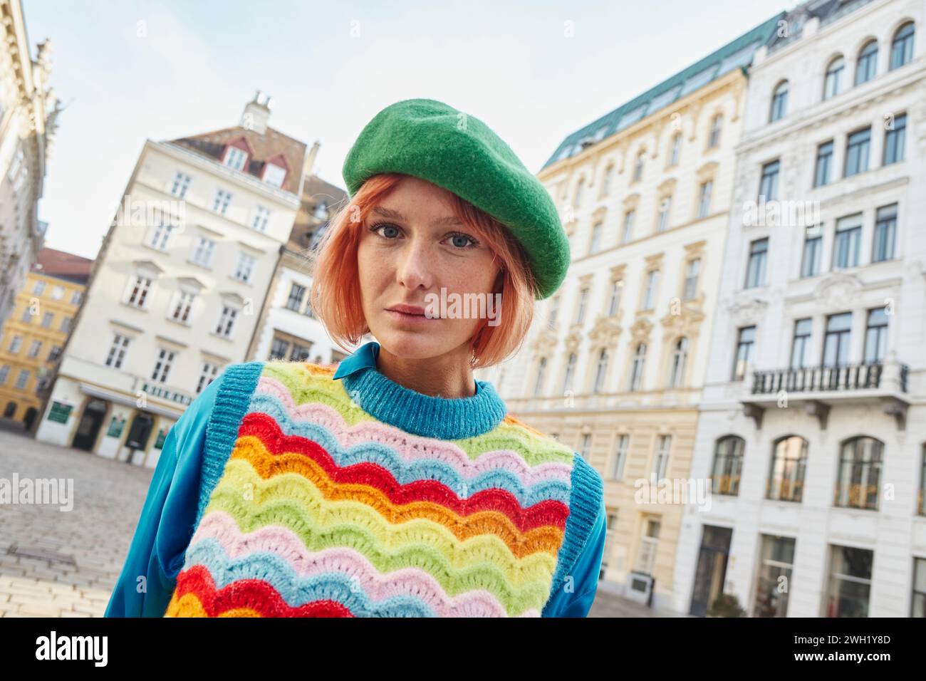 Moderna Street fashion, donna alla moda in berretto e gilet luminoso che guarda la macchina fotografica in strada a Vienna Foto Stock