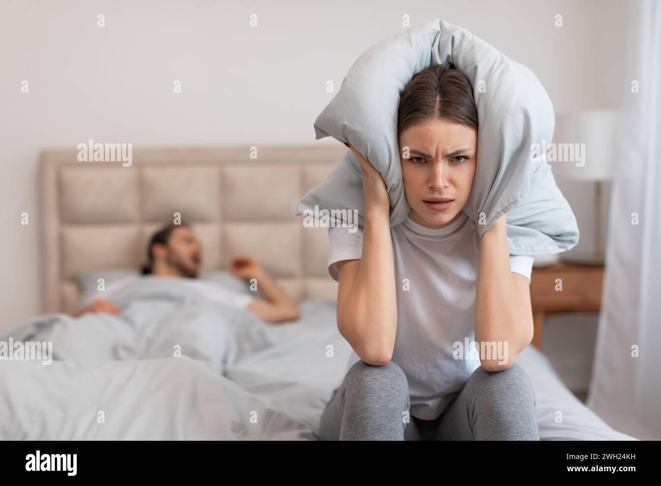 Donna che copre le orecchie con cuscino, uomo russare Foto Stock