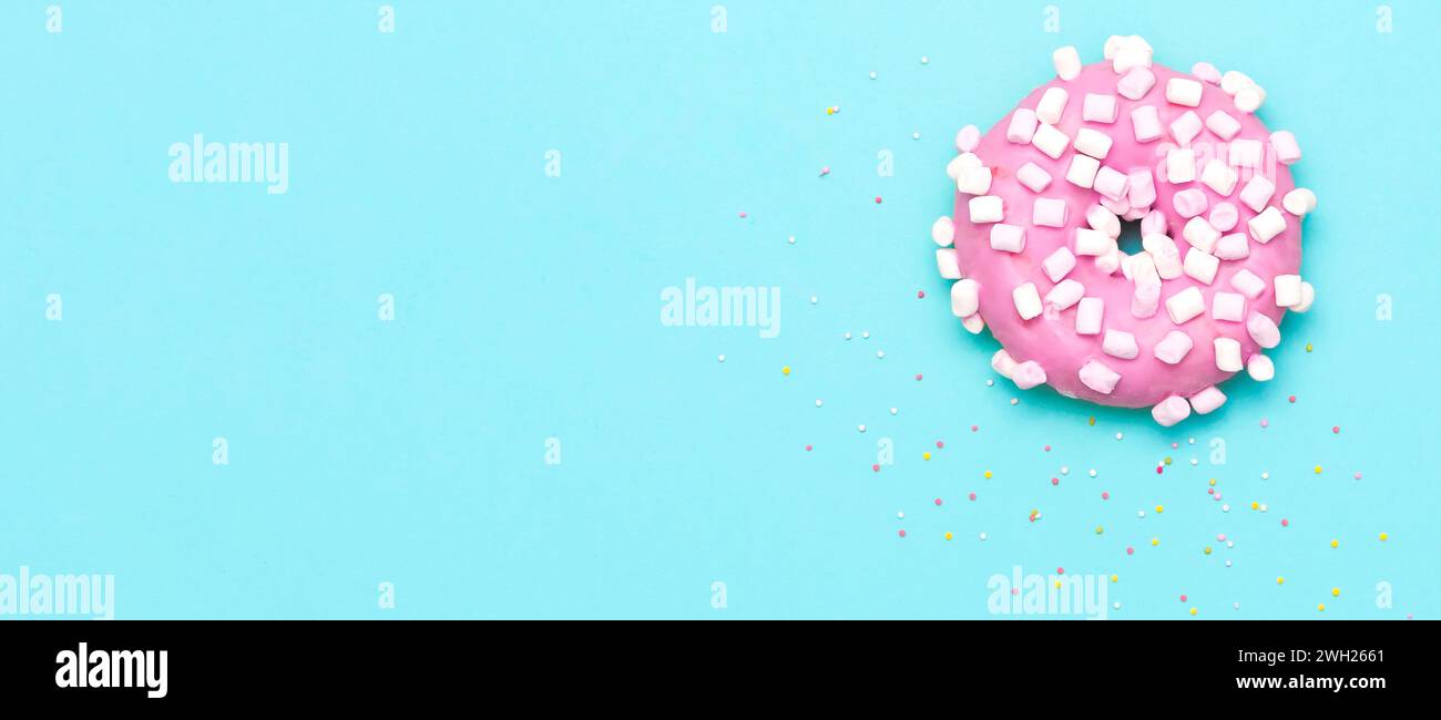 Ciambella rosa con murshmallow e sprinkles, vista dall'alto su sfondo blu Foto Stock