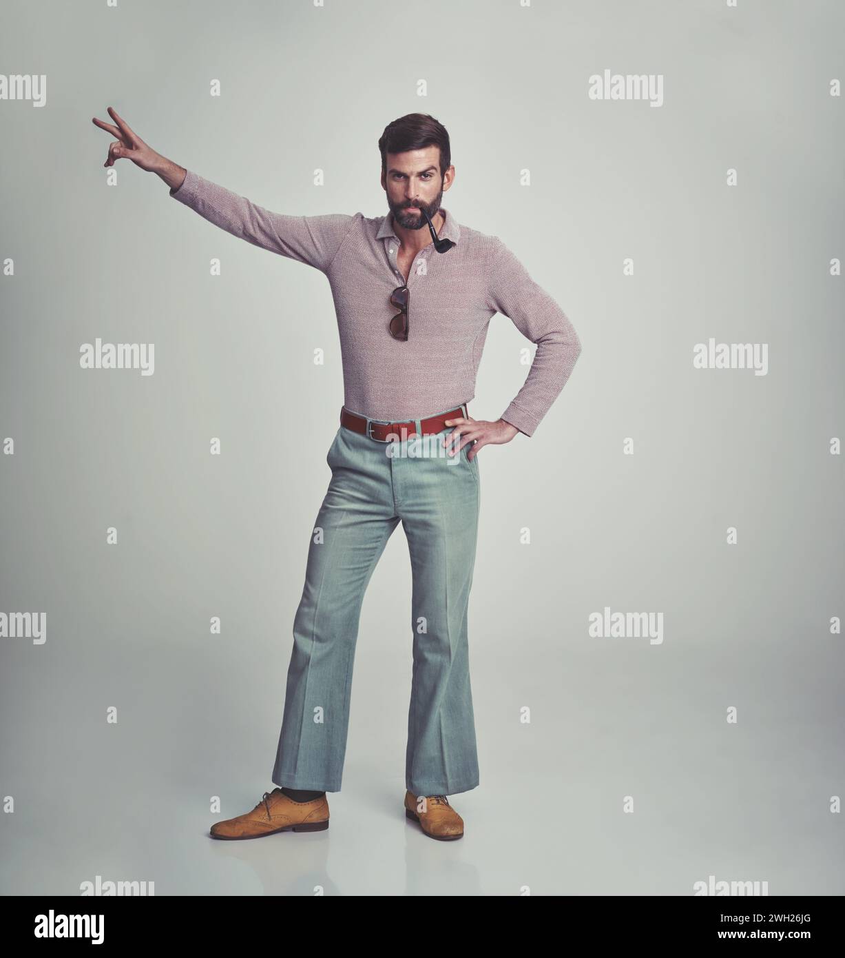 anni '70, moda e ritratto dell'uomo con un'estetica retrò o vintage su sfondo grigio dello studio. Fumare, pipa e persona ballare con pace e. Foto Stock