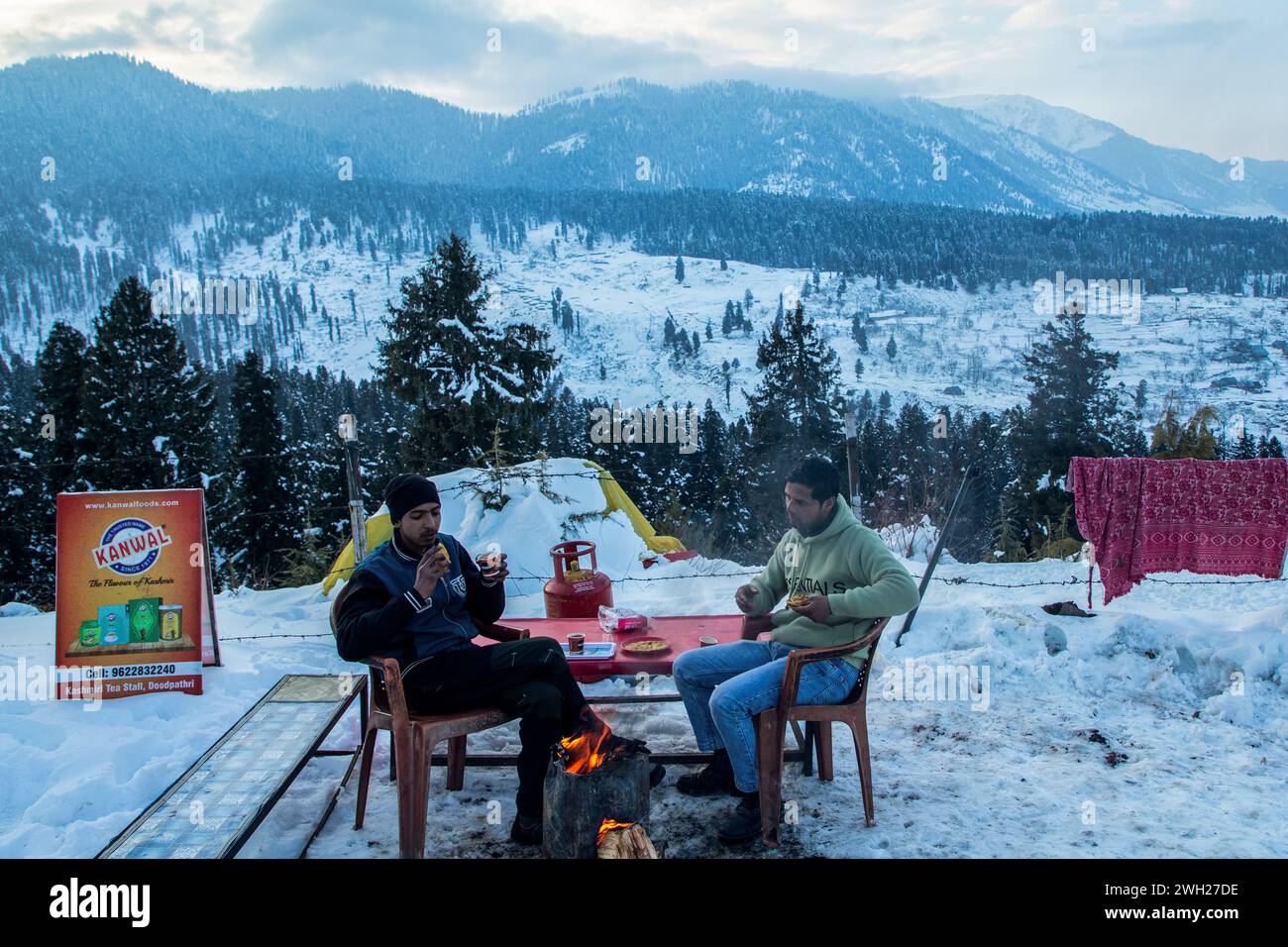 Srinagar, India. 7 febbraio 2024. I visitatori apprezzano il Noon Chai (tè salato) con tortillas di farina di mais in una stalla a lato della strada in una fredda giornata invernale dopo le forti nevicate a Doodhpathri, a circa 45 km a nord-est di Srinagar. Il tempo nella valle del Kashmir è migliorato dopo aver ricevuto nevicate fresche dopo un periodo di siccità. Tuttavia, le forti condizioni di ondate fredde continuano in Kashmir, con temperature minime che rimangono di diversi gradi al di sotto del congelamento nella maggior parte delle aree della regione, secondo i funzionari meteorologici. Credito: SOPA Images Limited/Alamy Live News Foto Stock