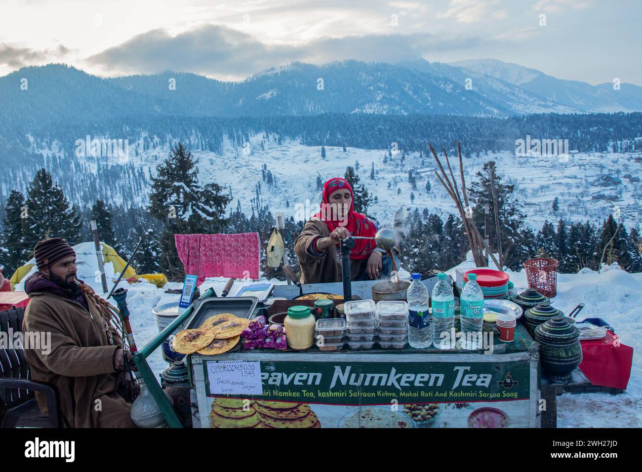 Una donna del Kashmir prepara il 'Noon Chai' (tè salato) e lo serve con tortillas di farina di mais ai turisti che passano accanto alla sua bancarella lungo la strada Doodhpathri in una fredda giornata invernale. Il tempo nella valle del Kashmir è migliorato dopo aver ricevuto nevicate fresche dopo un periodo di siccità. Tuttavia, le forti condizioni di ondate fredde continuano in Kashmir, con temperature minime che rimangono di diversi gradi al di sotto del congelamento nella maggior parte delle aree della regione, secondo i funzionari meteorologici. (Foto di Faisal Bashir / SOPA Images/Sipa USA) Foto Stock