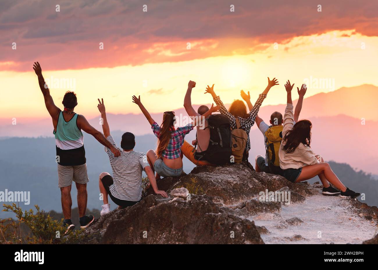 Un grande gruppo di giovani amici felici gode di un tramonto colorato sulla cima della montagna Foto Stock