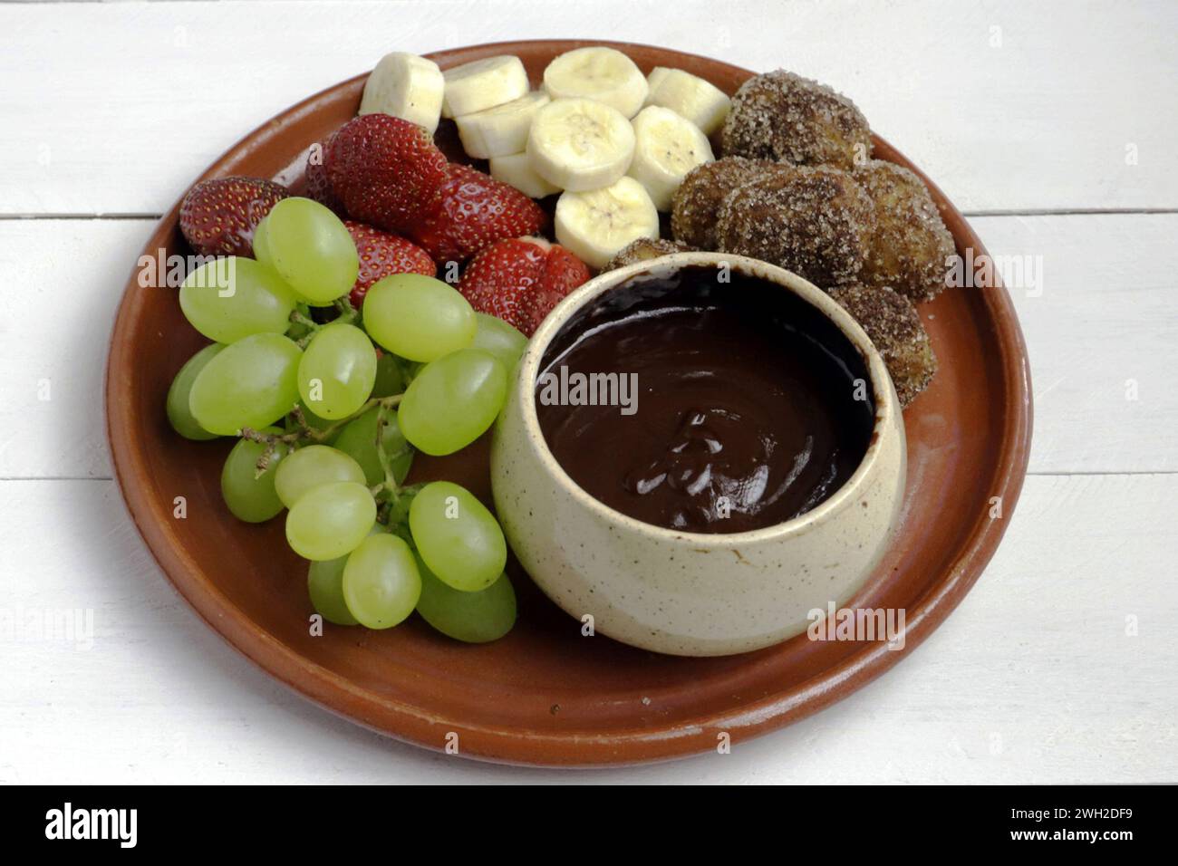 Una deliziosa fonduta al cioccolato servita con churros croccanti, uva fresca, fragole e banana. Foto Stock