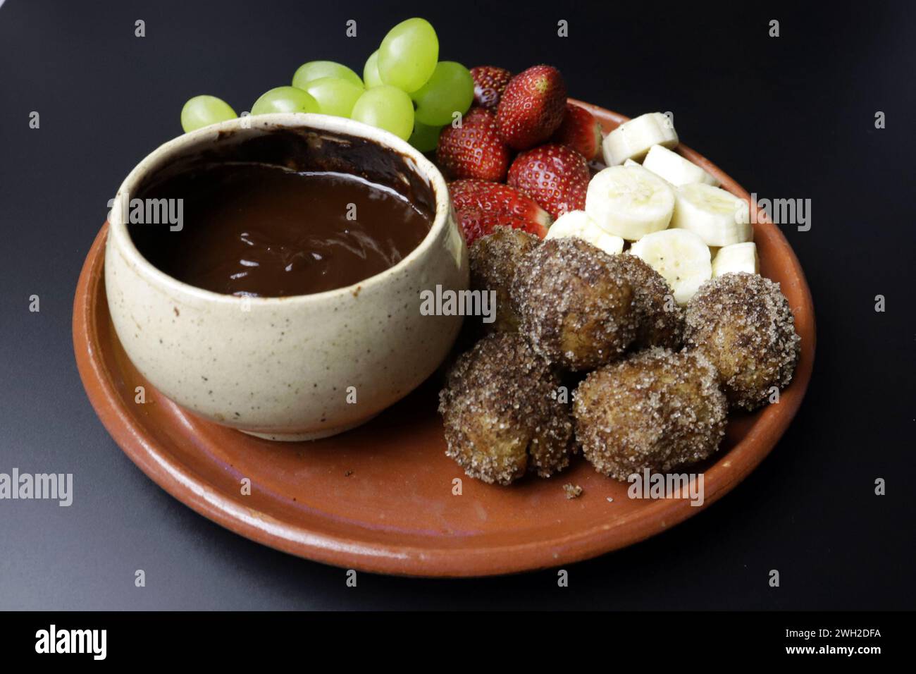Una deliziosa fonduta al cioccolato servita con churros croccanti, uva fresca, fragole e banana. Foto Stock