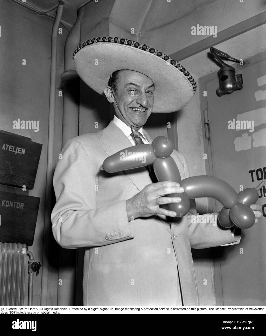 Intrattenimento negli anni '1950 Il Variety artist messicano Senor Carlos, vestito con un sombrero messicano, mostra felicemente la sua figura fatta con palloncini gonfiati. È riuscito a formare un cane con i palloncini. Il trucco consiste nel ruotare il palloncino in pezzi più piccoli e unire diversi pezzi per creare una figura. 1952. Kristoffersson 33K-3 Foto Stock