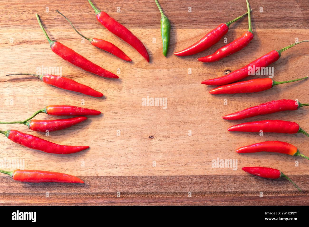 Gruppo di peperoncini rossi e un peperoncino verde disposti a semicerchio su una tavola di legno. Foto Stock