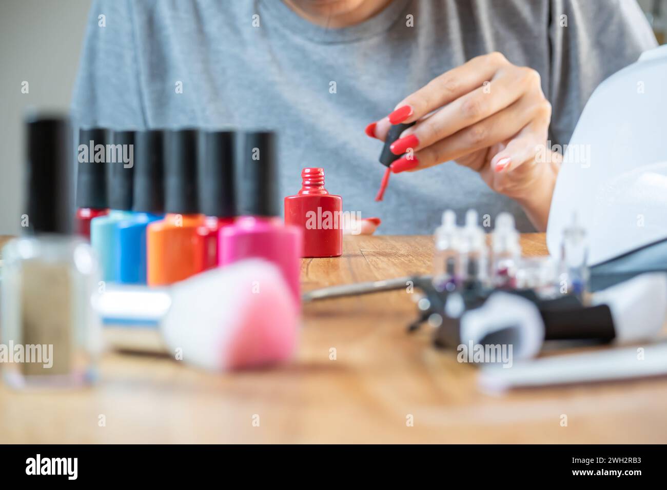 La donna si dipinge le unghie a tavola a casa. Ha molti colori smalti tra cui scegliere. Foto Stock