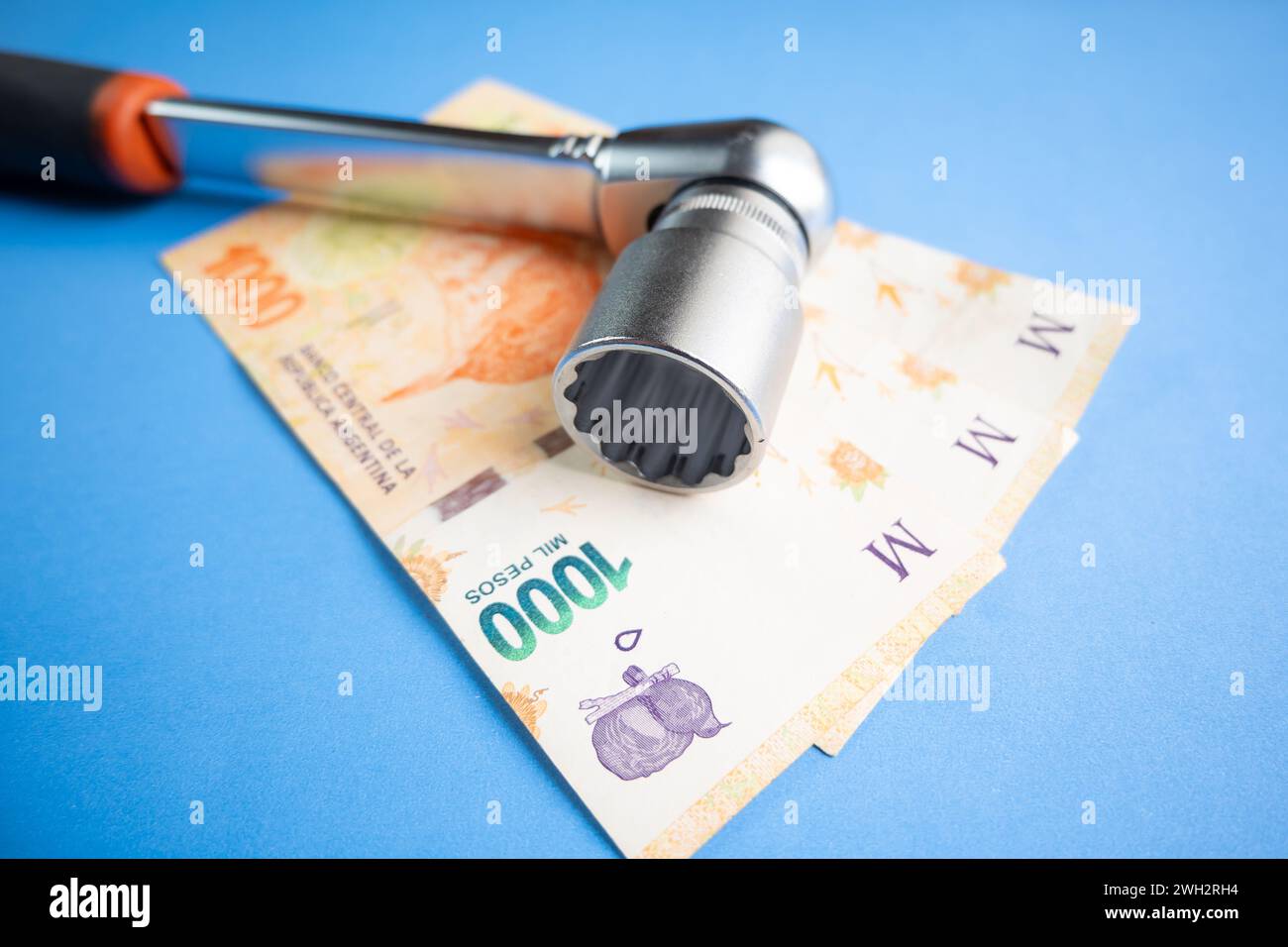 Pesos argentini serrati con una chiave a cricchetto su sfondo blu. Foto Stock