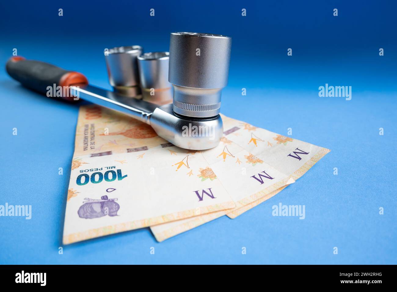 Concetto del costo dei meccanici realizzati con una chiave a cricchetto e banconote in peso argentino su sfondo blu. Foto Stock