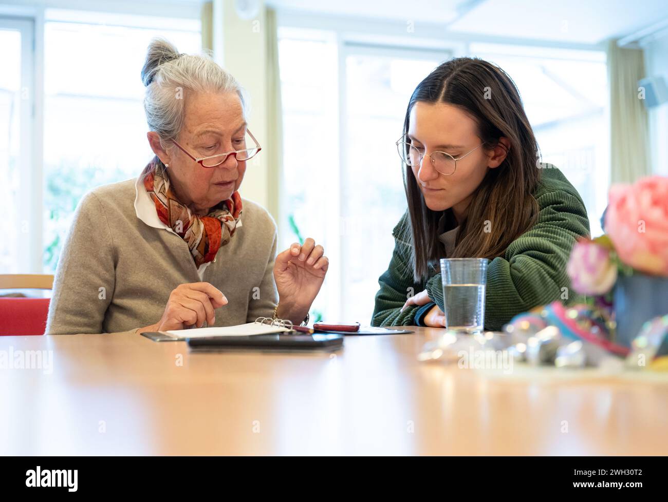 Monaco, Germania. 7 febbraio 2024. Katrin (r) risponde alle (l) domande di Helga sull'iPhone Apple durante la consultazione con gli anziani sullo smartphone. Dal 2021, la Caritas offre ore di consultazione in cui gli anziani possono ottenere aiuto per problemi con i loro telefoni cellulari. L'associazione sta cercando urgentemente più consulenti per questi orari di consultazione. Credito: Lukas Barth/dpa/Alamy Live News Foto Stock