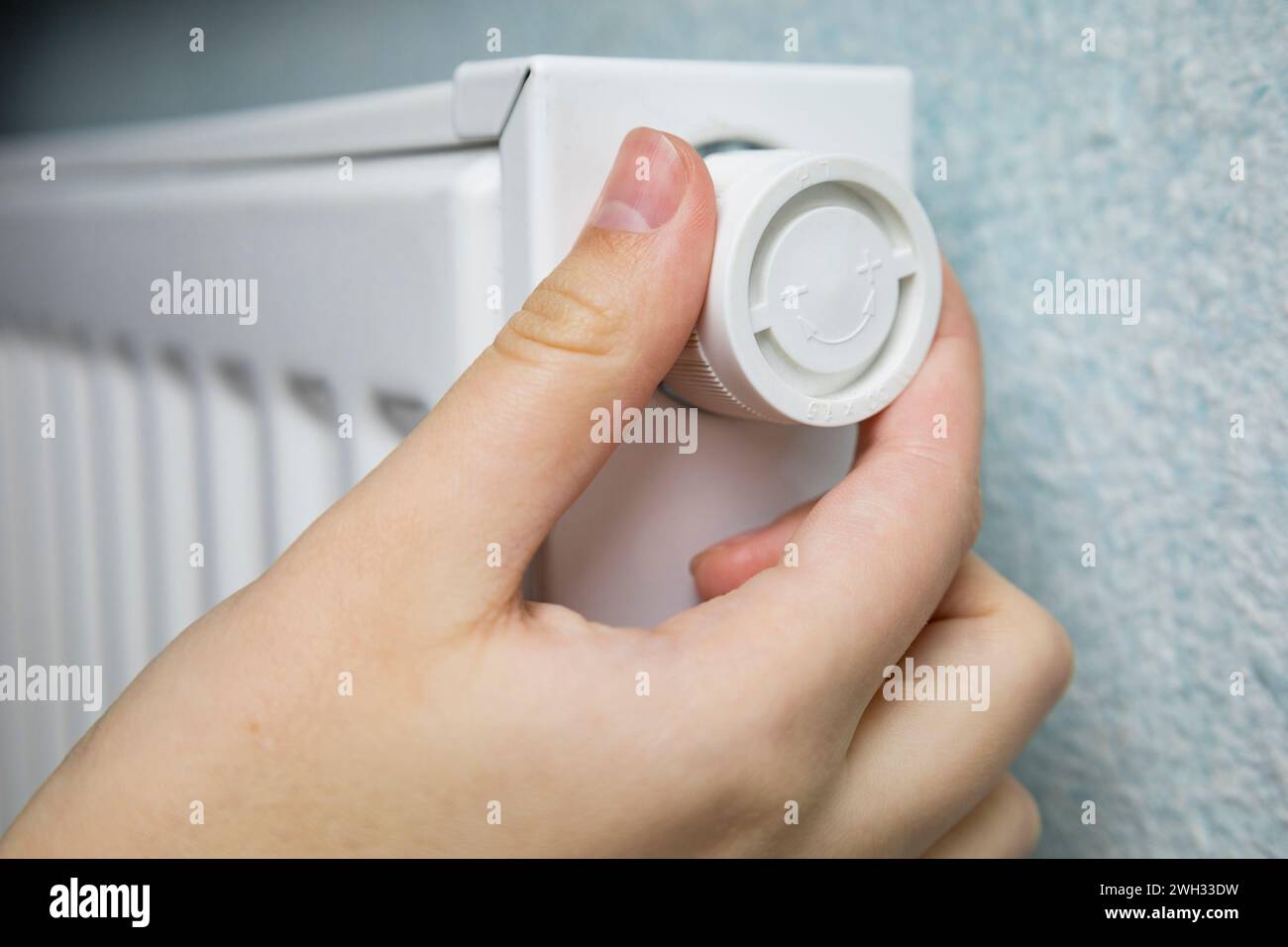 Donna regola il riscaldamento sul radiatore bianco della batteria a casa nella fredda stagione invernale, mani da vicino. Riscaldamento centralizzato in un edificio moderno ben tenuto. A. Foto Stock