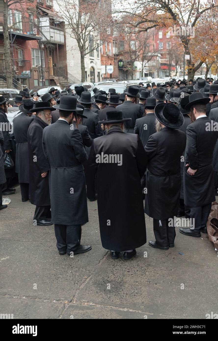 Un grande gruppo di ebrei ortodossi vestiti allo stesso modo ascolta un discorso all'aperto. A Brooklyn, New York. Foto Stock