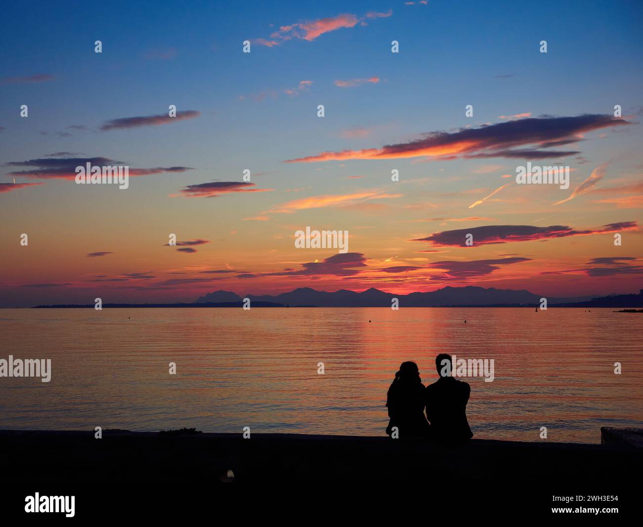 Romantico tramonto sulla baia di Cannes, Riviera, Francia, con una giovane coppia seduta e sagomata sul mare rosa. Foto Stock