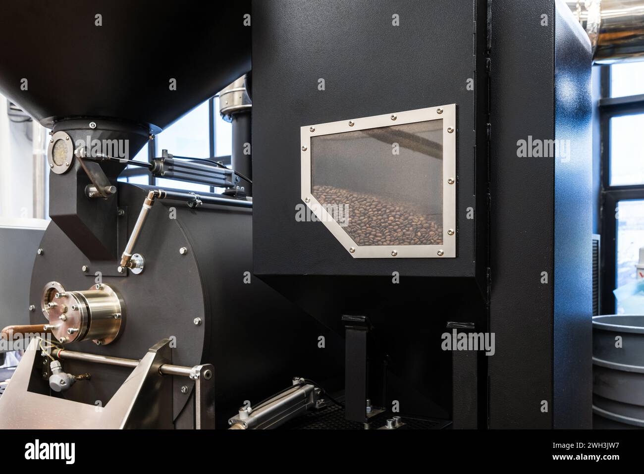 Foto ravvicinata della torrefazione industriale nera, i semi di caffè tostati sono dietro la finestra tecnologica Foto Stock