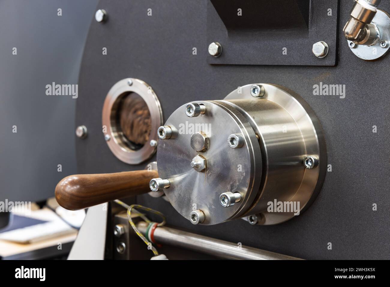 Foto ravvicinata della torrefazione industriale, i semi di caffè tostati si trovano all'interno dietro una piccola finestra tecnologica rotonda Foto Stock