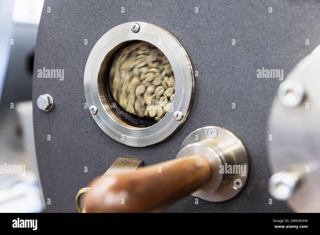 Foto ravvicinata della torrefazione industriale, semi verdi si trovano all'interno dietro una piccola finestra tecnologica rotonda Foto Stock