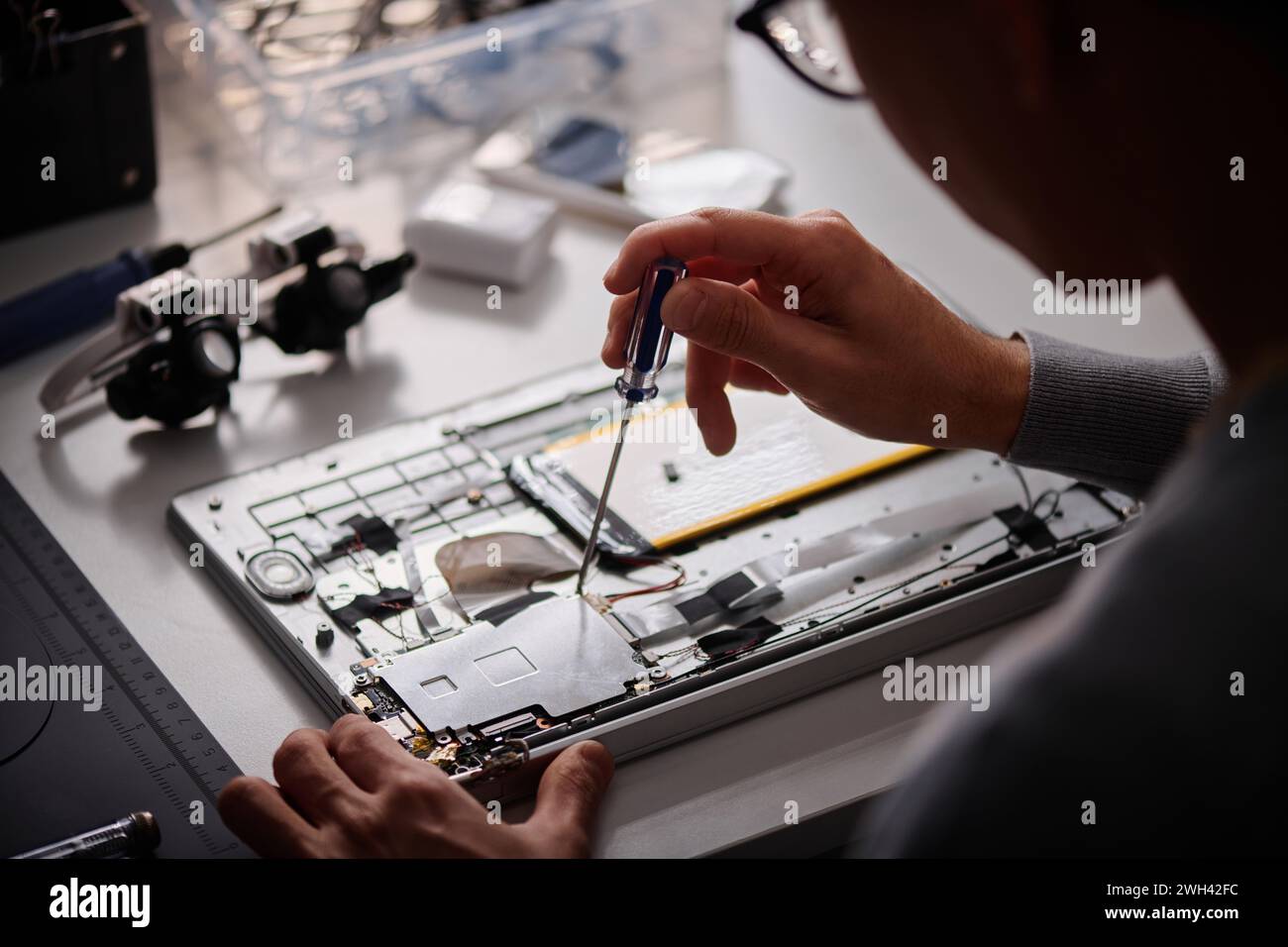 Tecnico maschile irriconoscibile che ripara il computer utilizzando un cacciavite in un'officina moderna Foto Stock