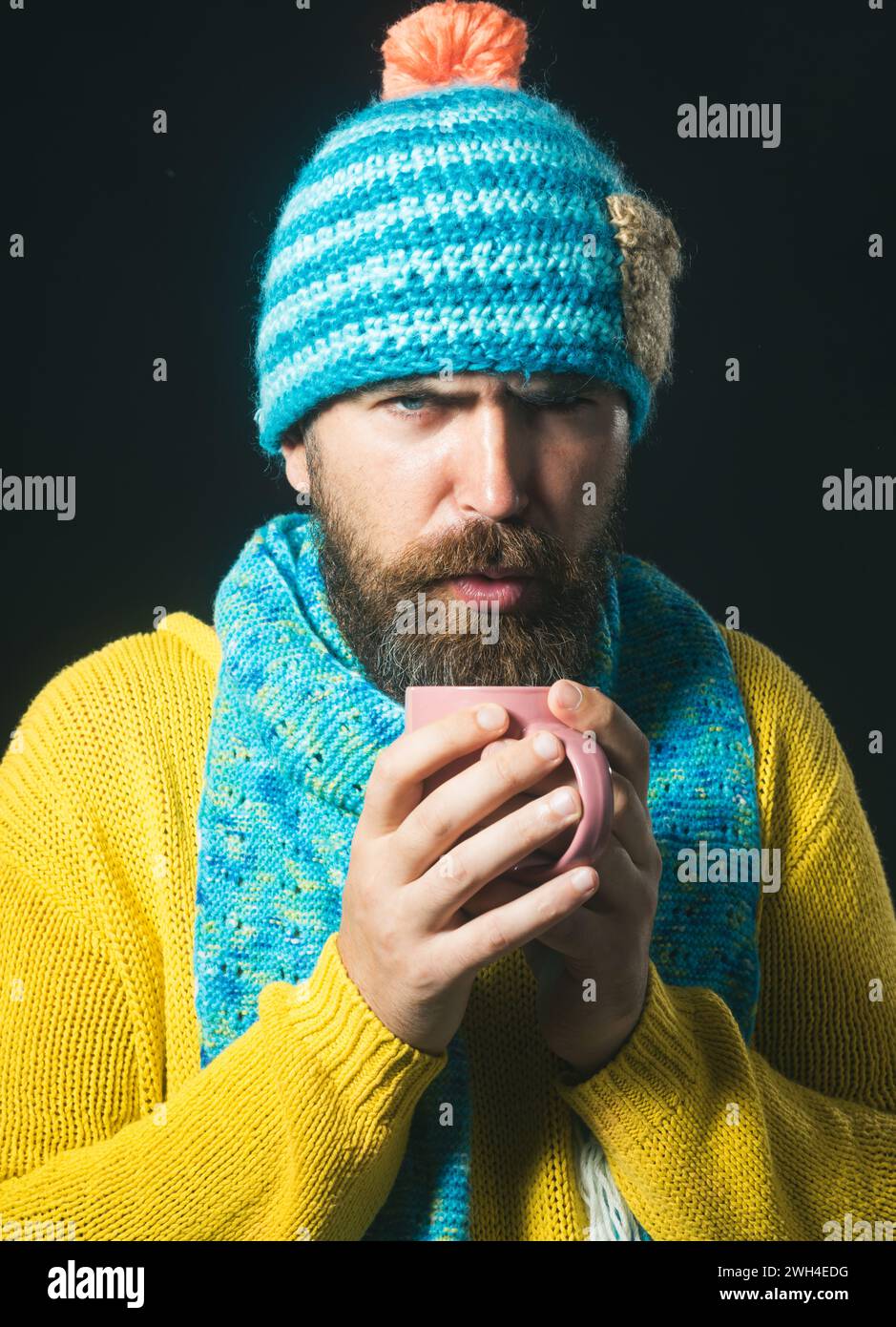 Uomo barbuto che soffia con caffè caldo o tè. Bell'uomo con barba e baffi soffia su una bevanda calda per raffreddarla. Ragazzo attraente con maglione giallo Foto Stock